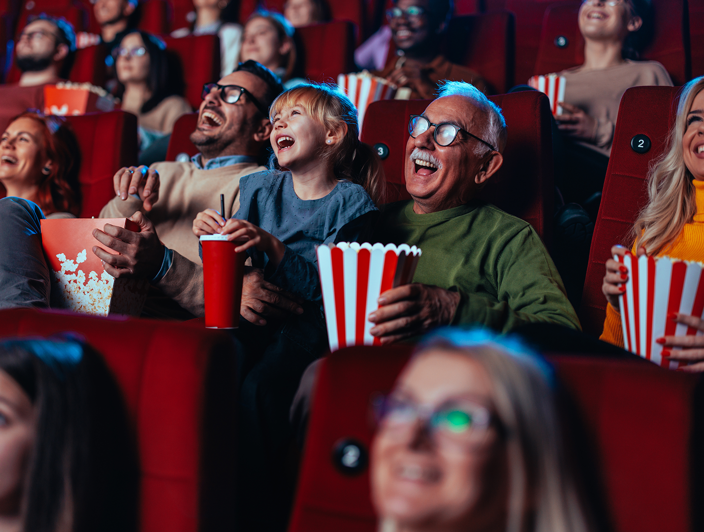 Vader, zoon en opa zitten naast elkaar in een theaterzaal en lachen.